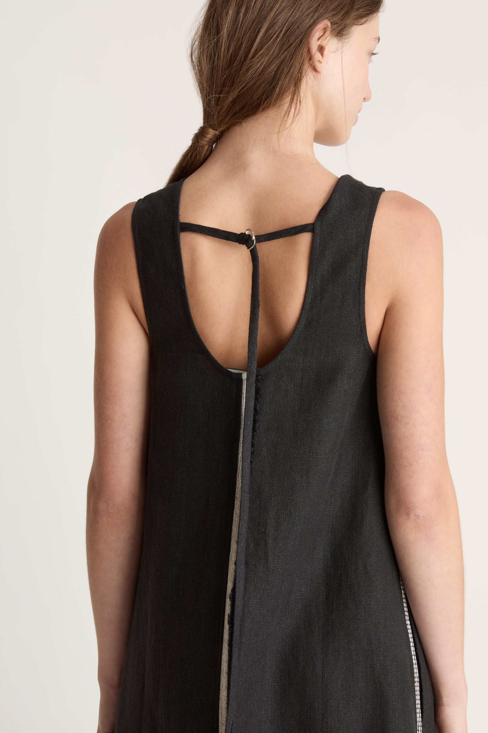 Woman wearing a black sleeveless dress with astripe down the front on a white background