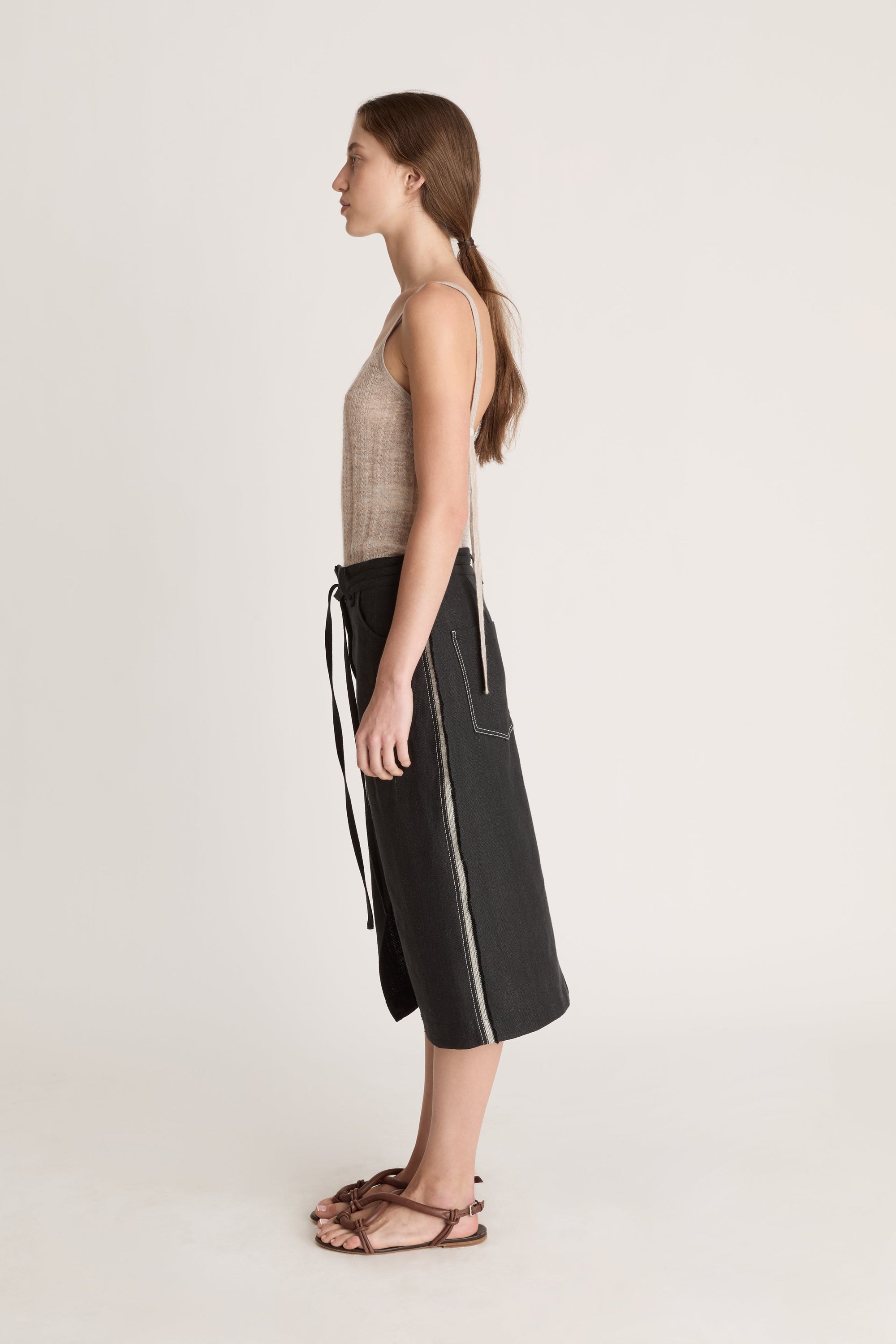 Woman wearing a beige tank top and black wrap skirt on a white background