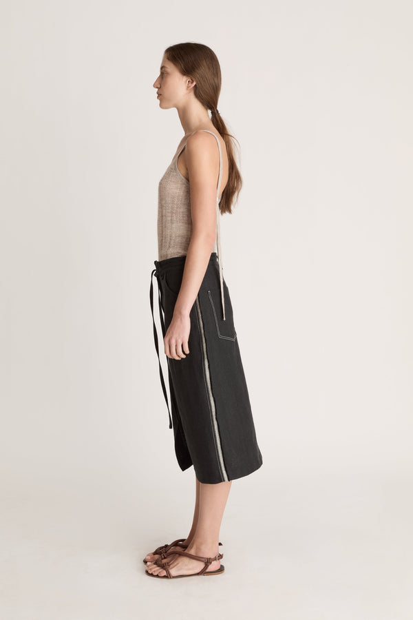 Woman wearing a beige tank top and black wrap skirt on a white background