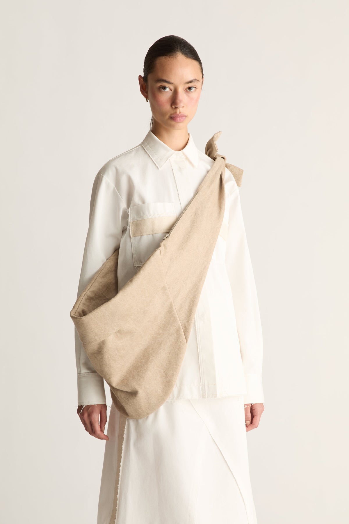 Angled view of a woman with hair pulled back carrying a large slouchy beige fabric shoulder bag over a white shirt