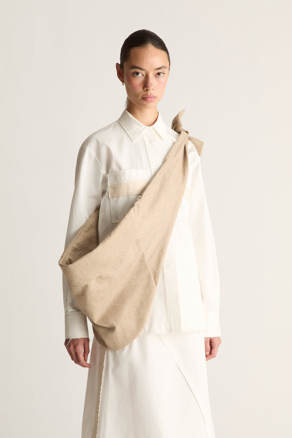 Angled view of a woman with hair pulled back carrying a large slouchy beige fabric shoulder bag over a white shirt
