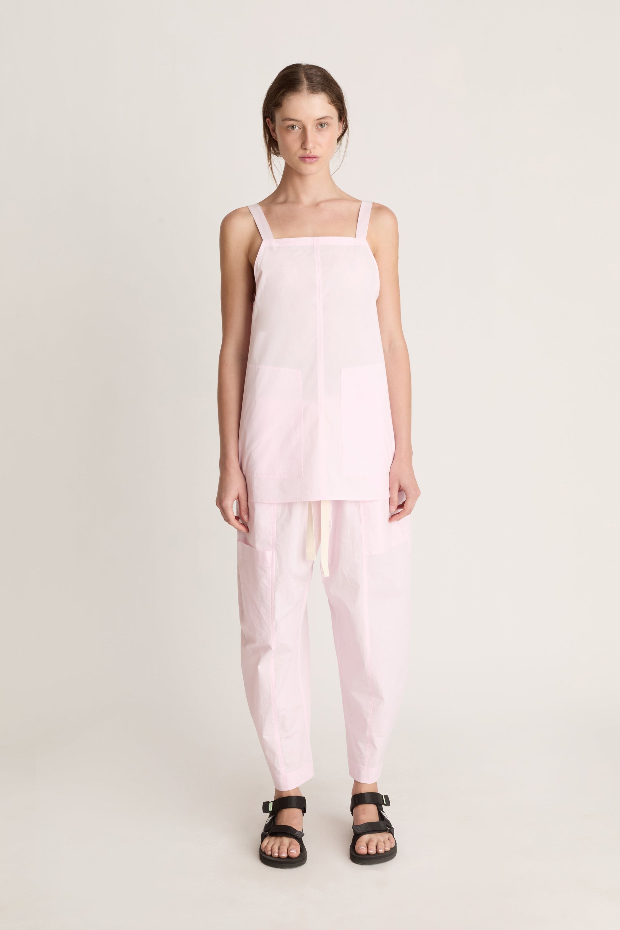 Woman wearing a light pink cami top and light pink pants on a white background