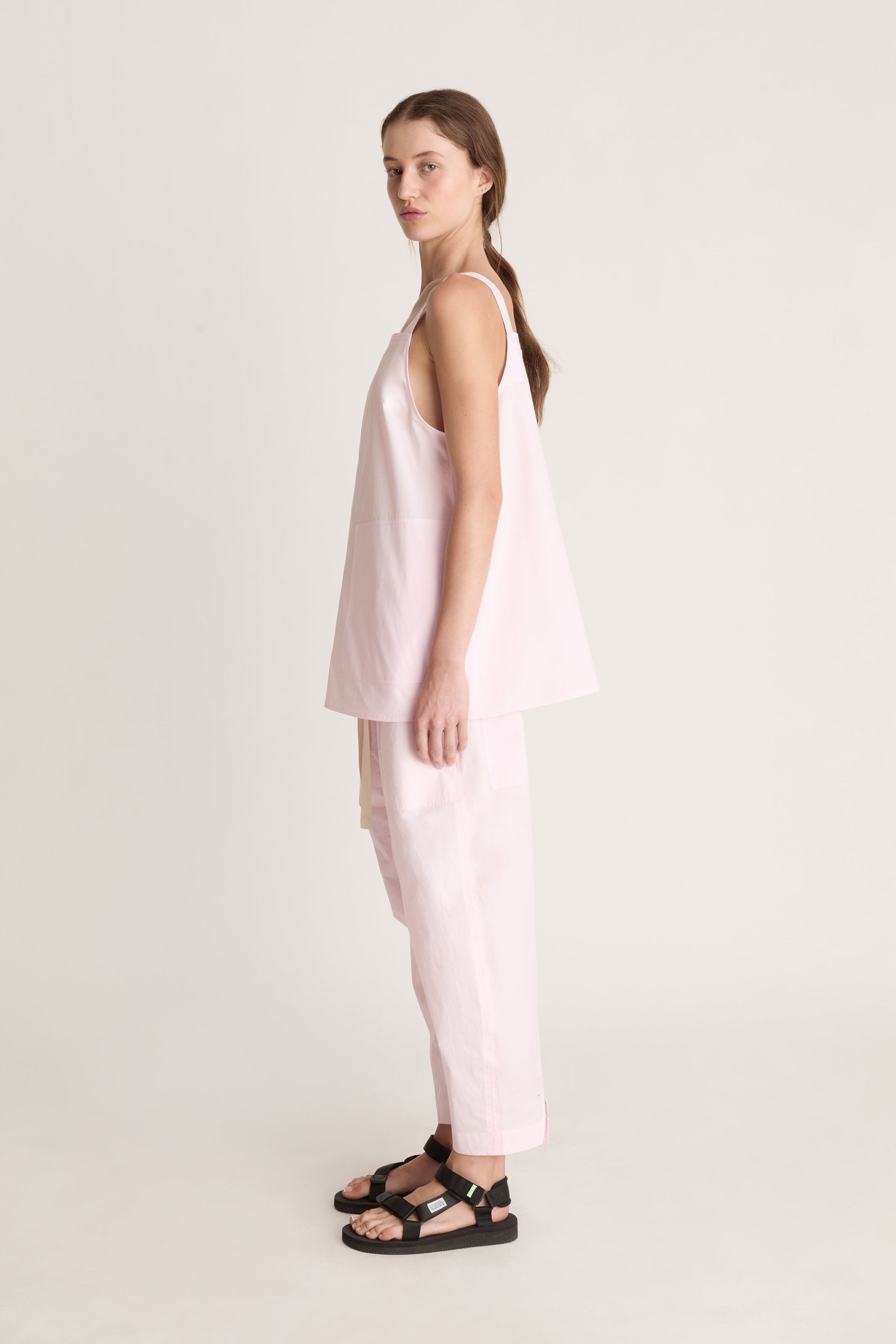 Woman wearing a light pink cami top and light pink pants on a white background