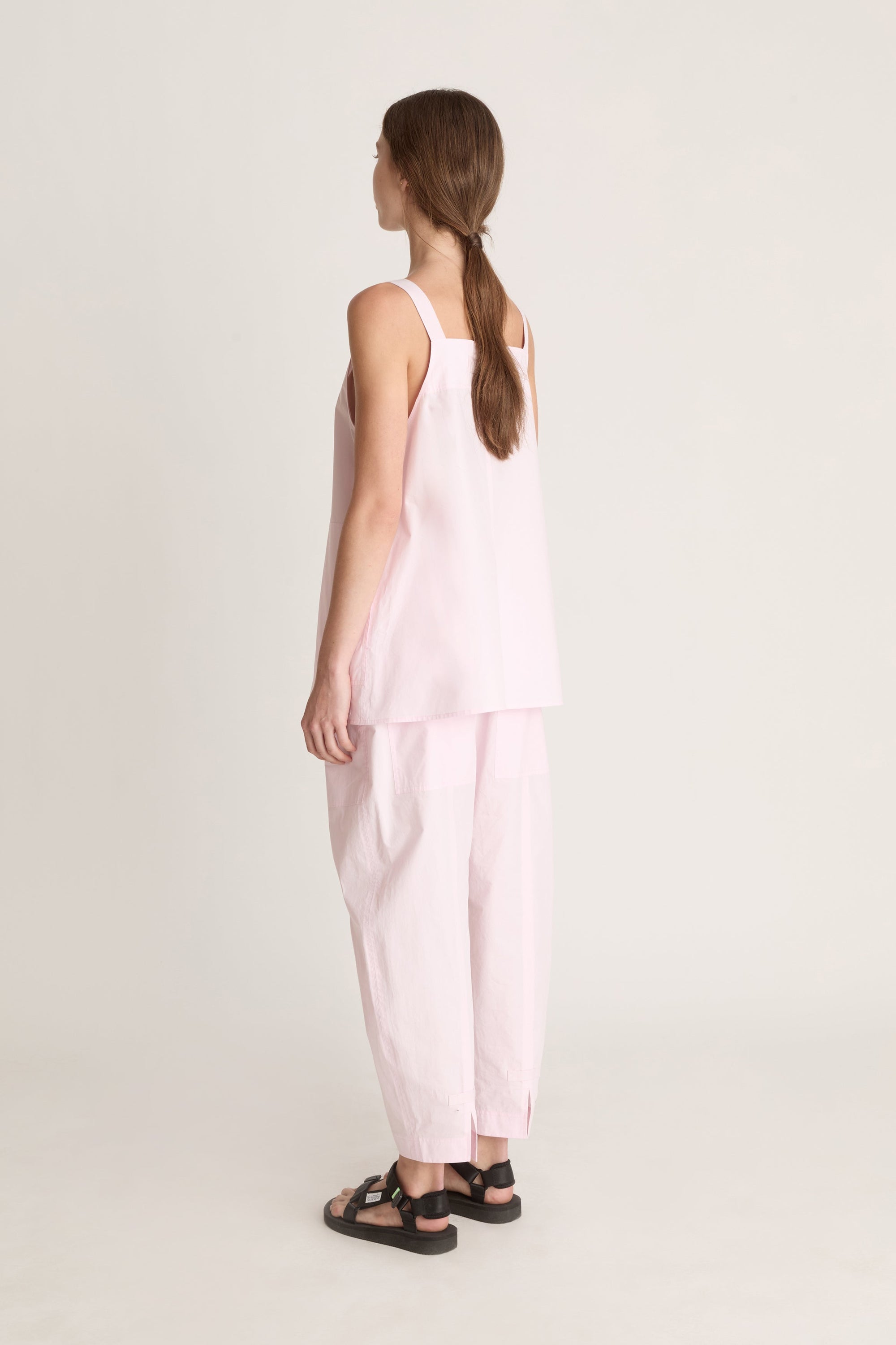 Woman wearing a light pink cami top and light pink pants on a white background