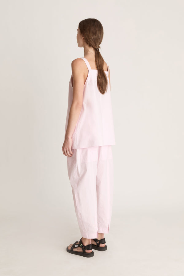 Woman wearing a light pink cami top and light pink pants on a white background