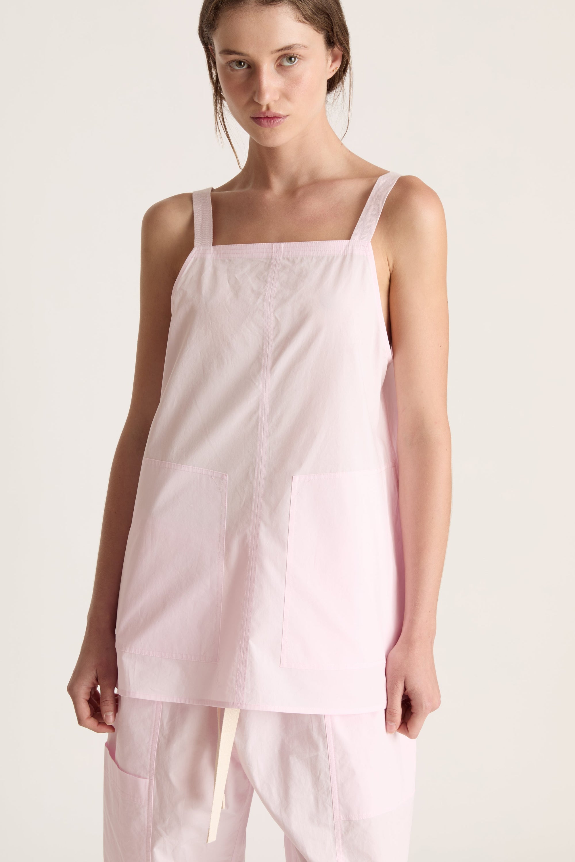 Woman wearing a light pink cami top and light pink pants on a white background