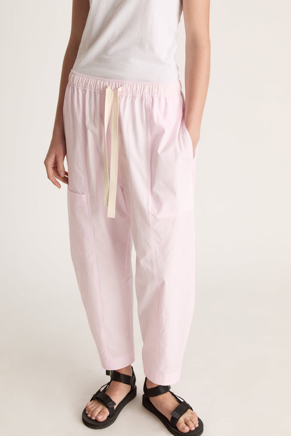 Woman wearing a white sleeveless top and light pink pants on a white background