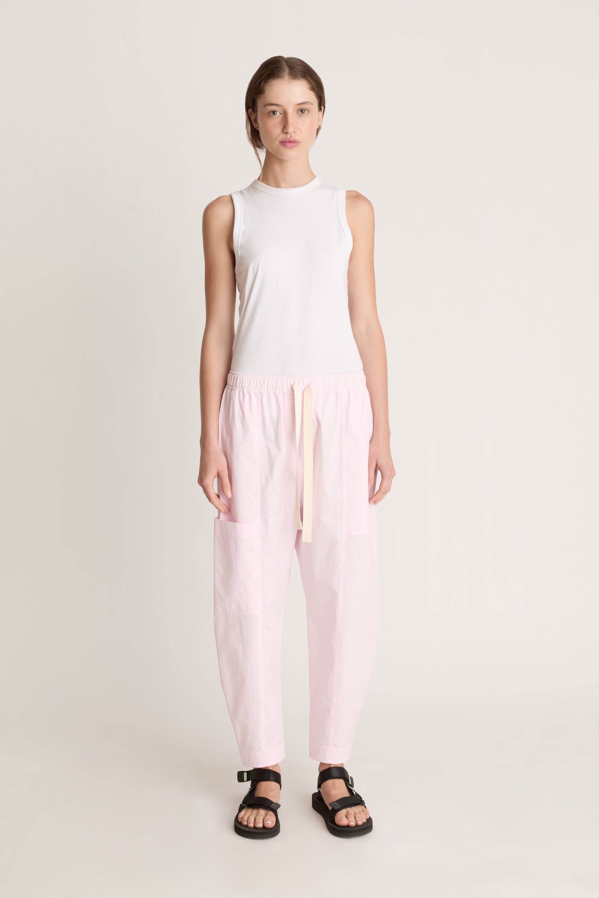 Woman wearing a white sleeveless top and light pink pants on a white background
