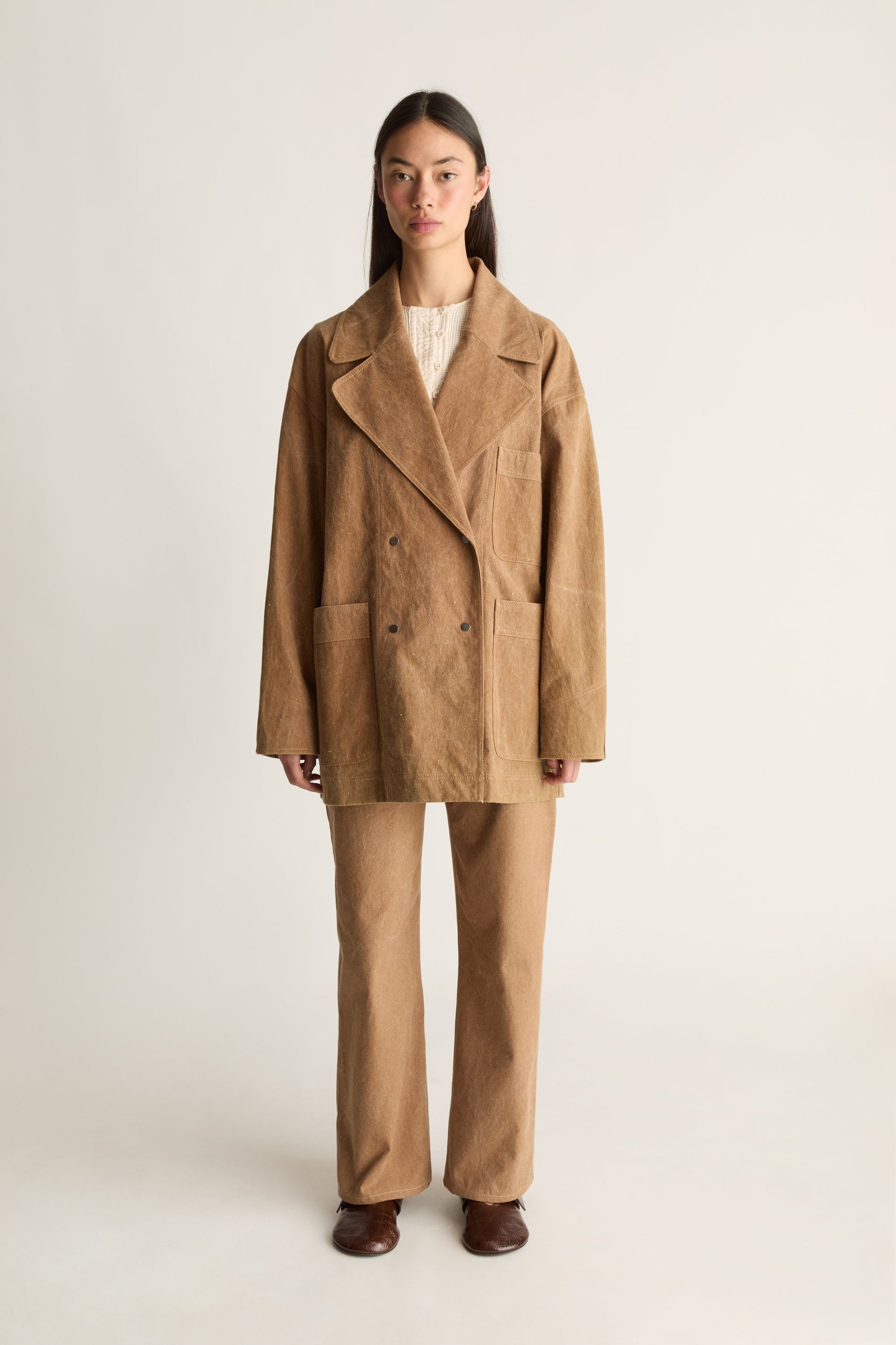 Woman wearing a brown coat and pants on a white background, facing the front.