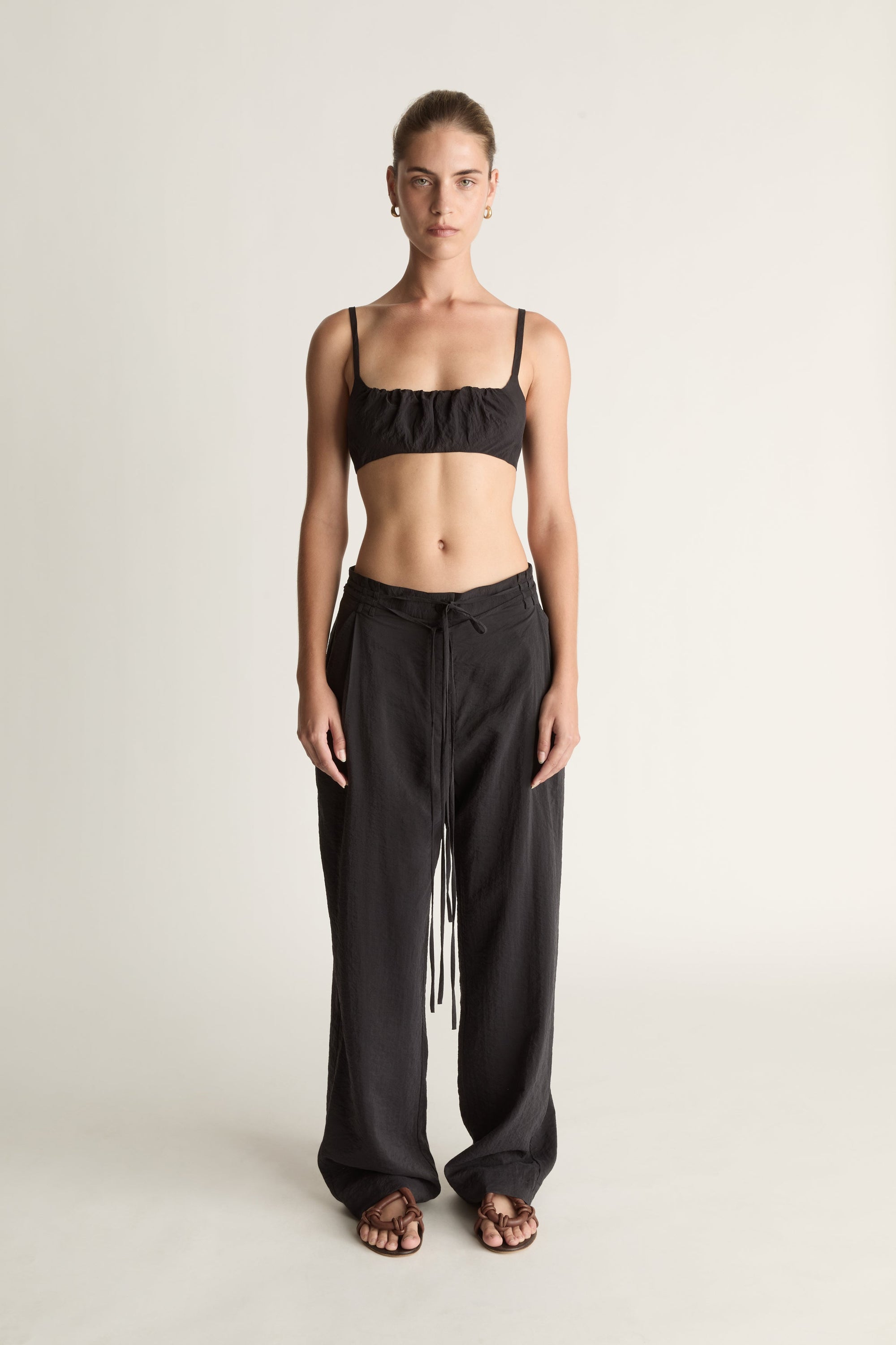 Woman wearing a cropped black top and wide-leg pants on a plain background