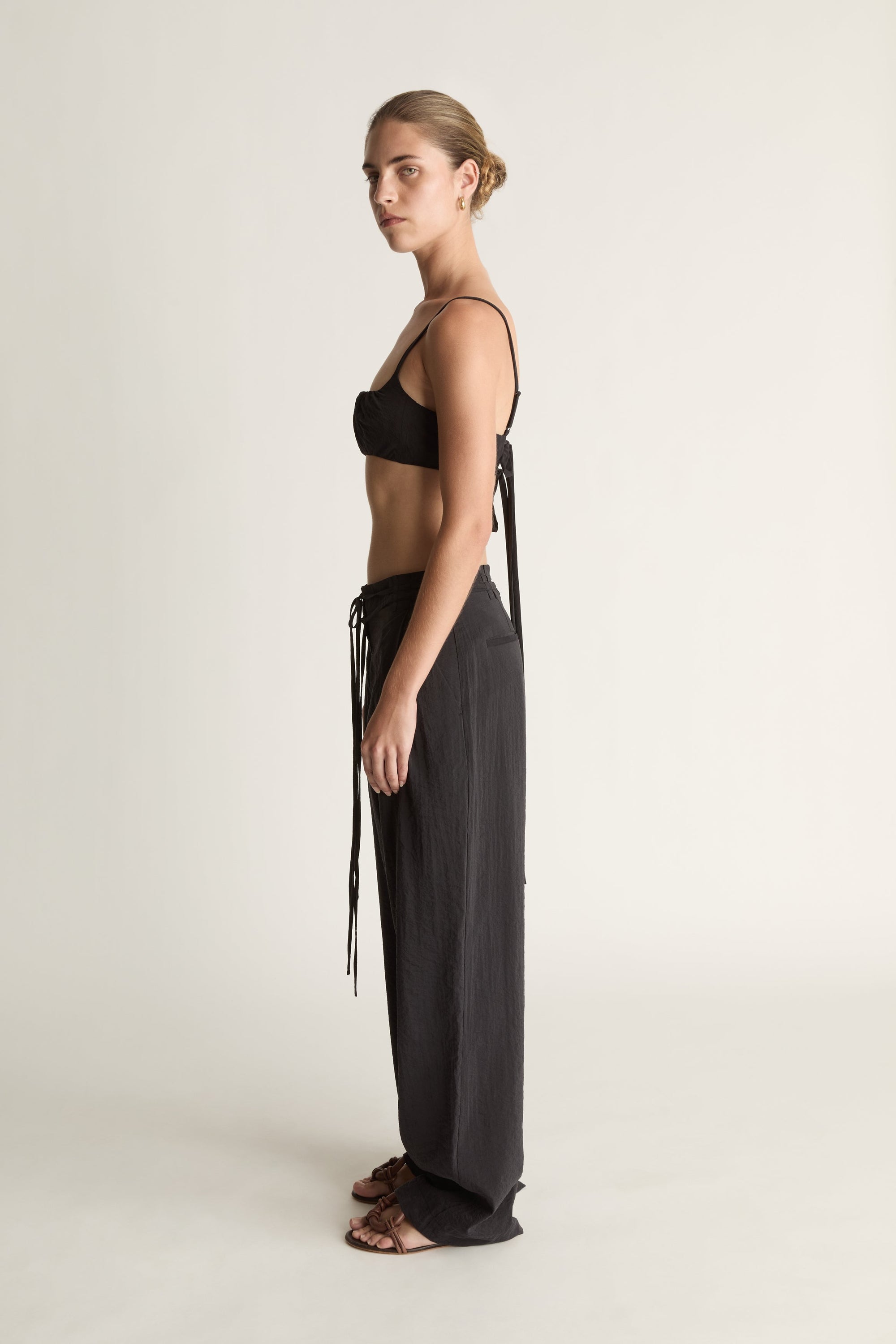 Woman wearing a cropped black top and wide-leg pants on a plain background