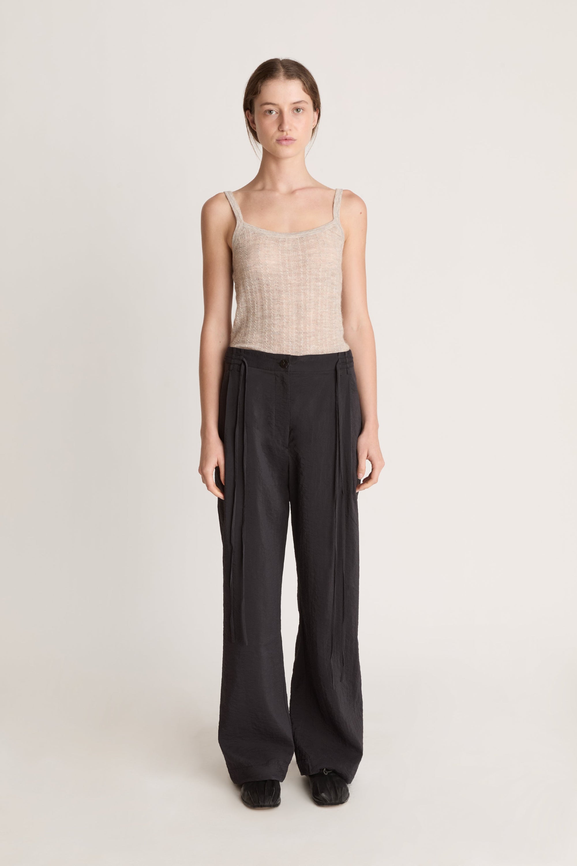 Woman wearing a beige tank top and black pants on a white background
