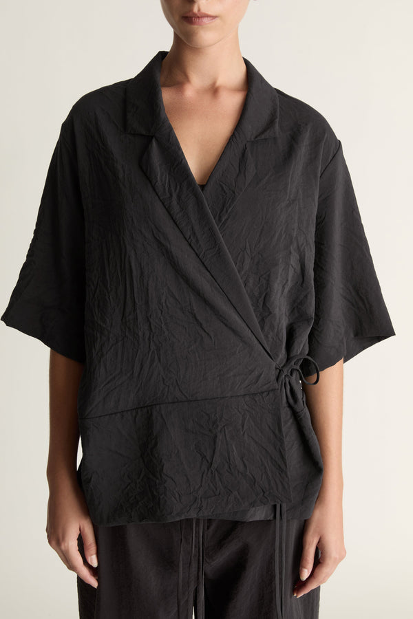 Person wearing a black wrap top with black trousers on a plain background