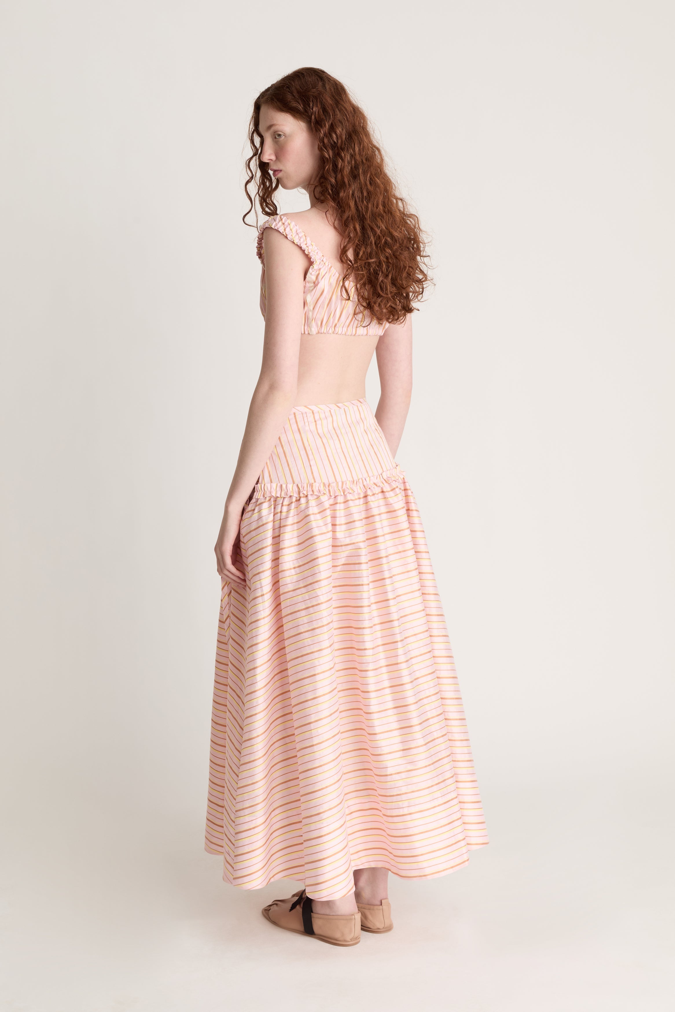 Woman wearing a pink striped crop top and skirt on a plain background