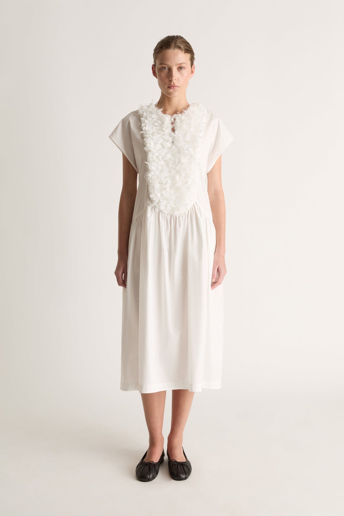 Front view of a white midi dress with cap sleeves, a ruffled bib front and gathered dropped waist.