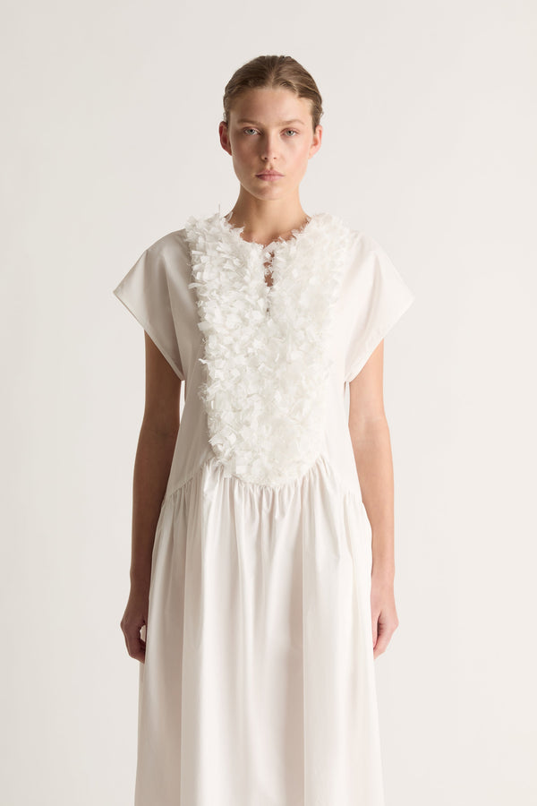 Close-up front view of a white dress with a textured ruffle bib, keyhole neckline and cap sleeves.