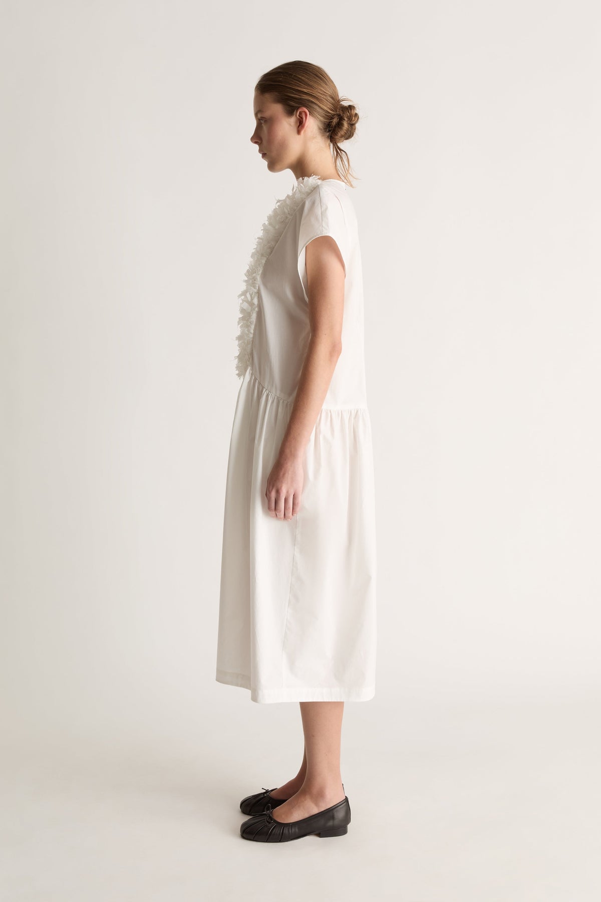 Side view of a white midi dress with cap sleeves, a ruffled front and gathered skirt.
