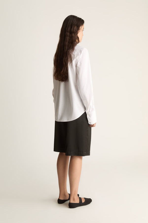 Back view of a woman with long wavy hair in a white shirt with curved hem and black knee-length shorts