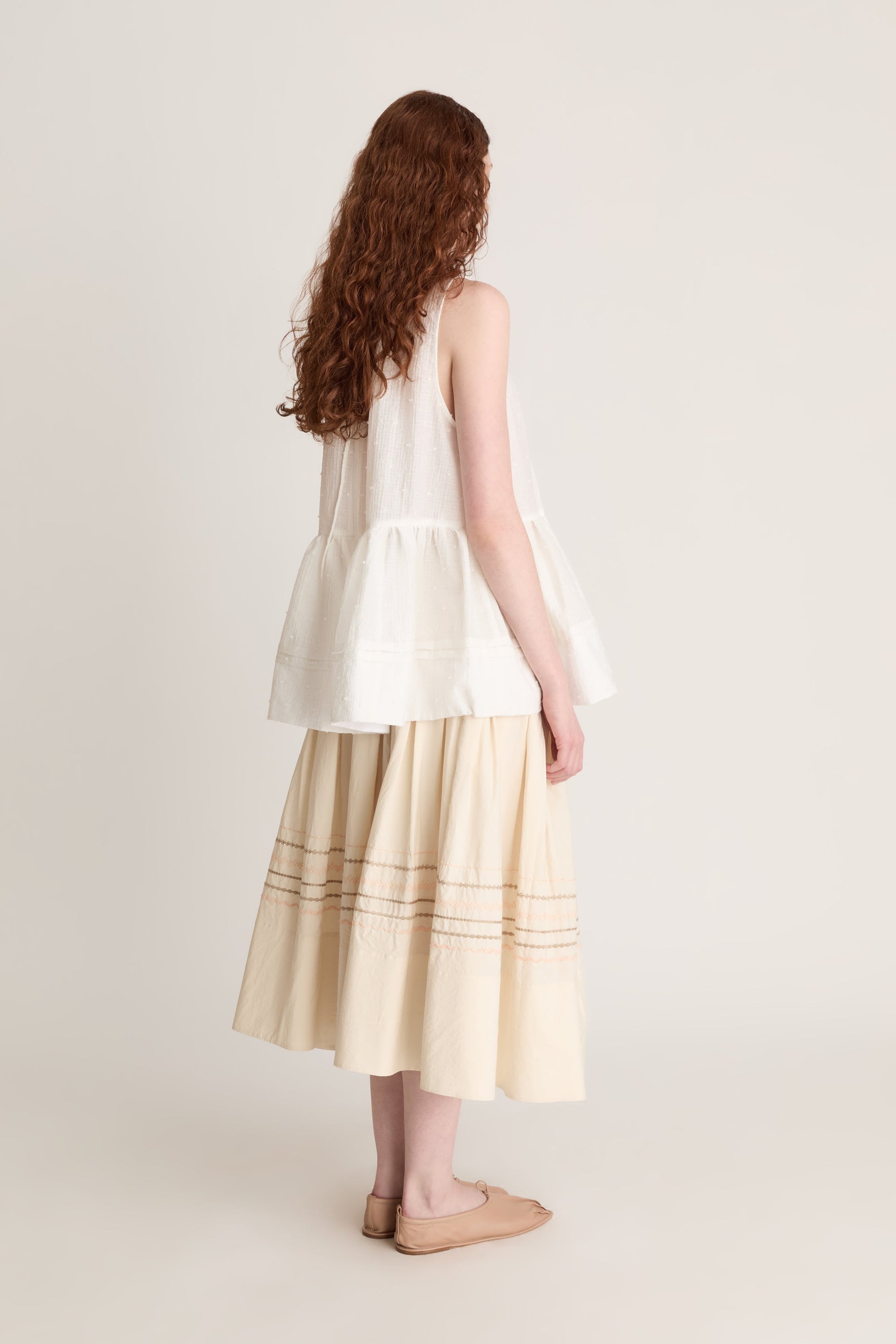 A woman wearing a white top with a peplum with a beige skirt on a white background