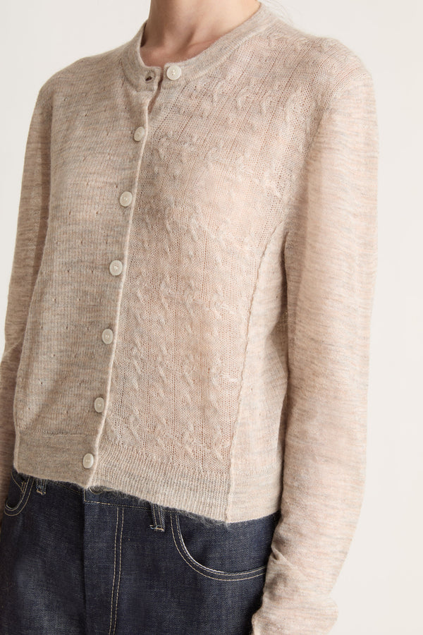 Person wearing a beige cardigan and dark jeans on a white background