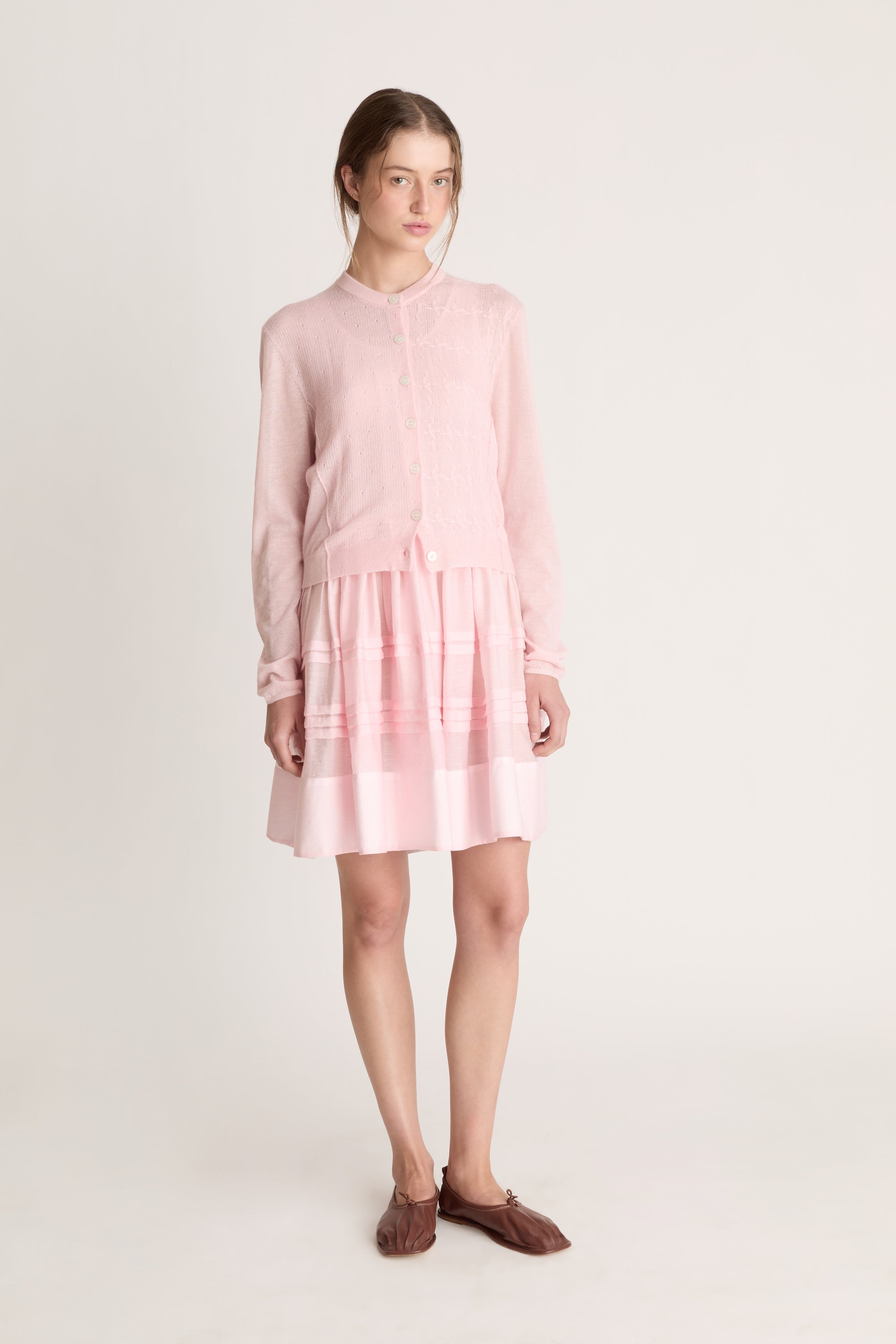 Woman wearing a light pink dress with a light pink knit cardigan on a white background