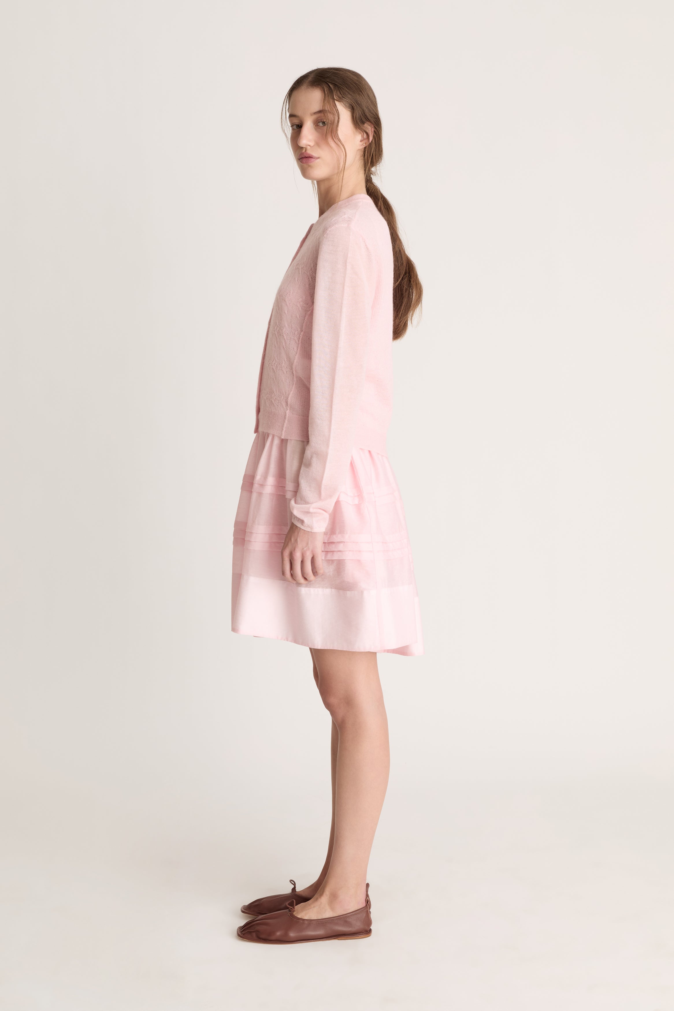 Woman wearing a light pink dress with a light pink knit cardigan on a white background