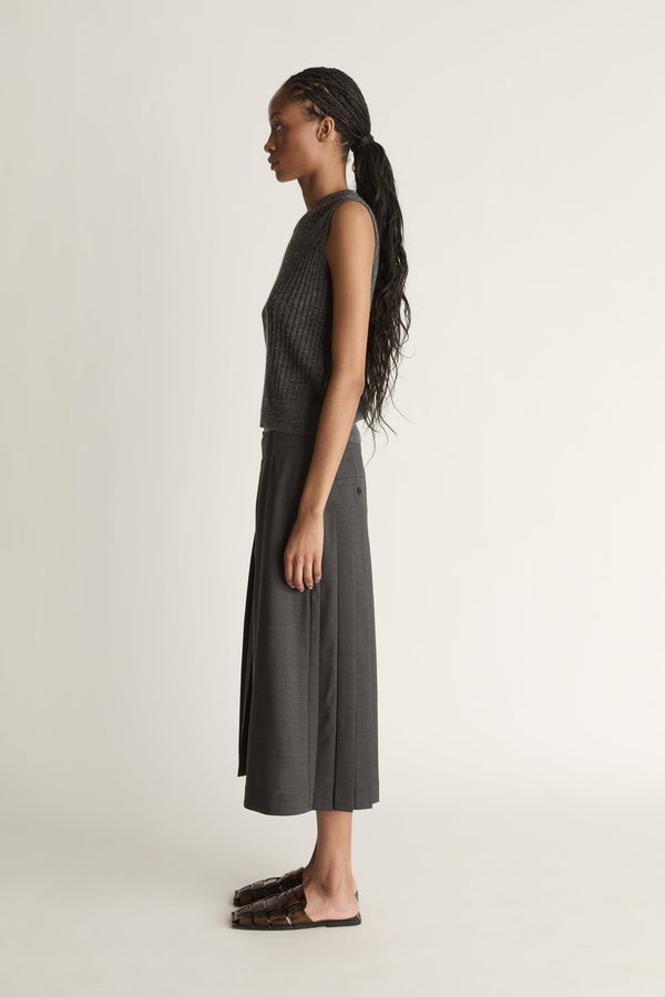 Woman wearing a dark gray sleeveless v neck knit top and skirt on a white background