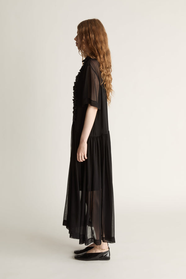 Woman wearing a black dress with sheer sleeves and lace details on a white background