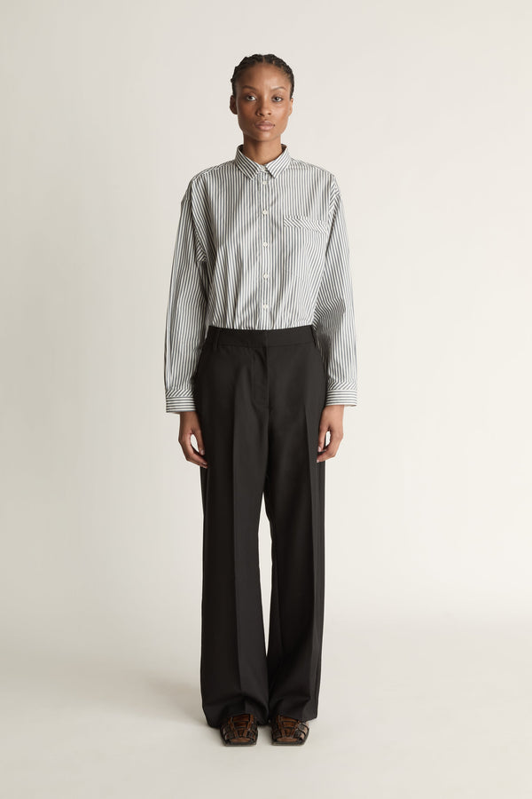 Person wearing a striped shirt and black pants on a white background
