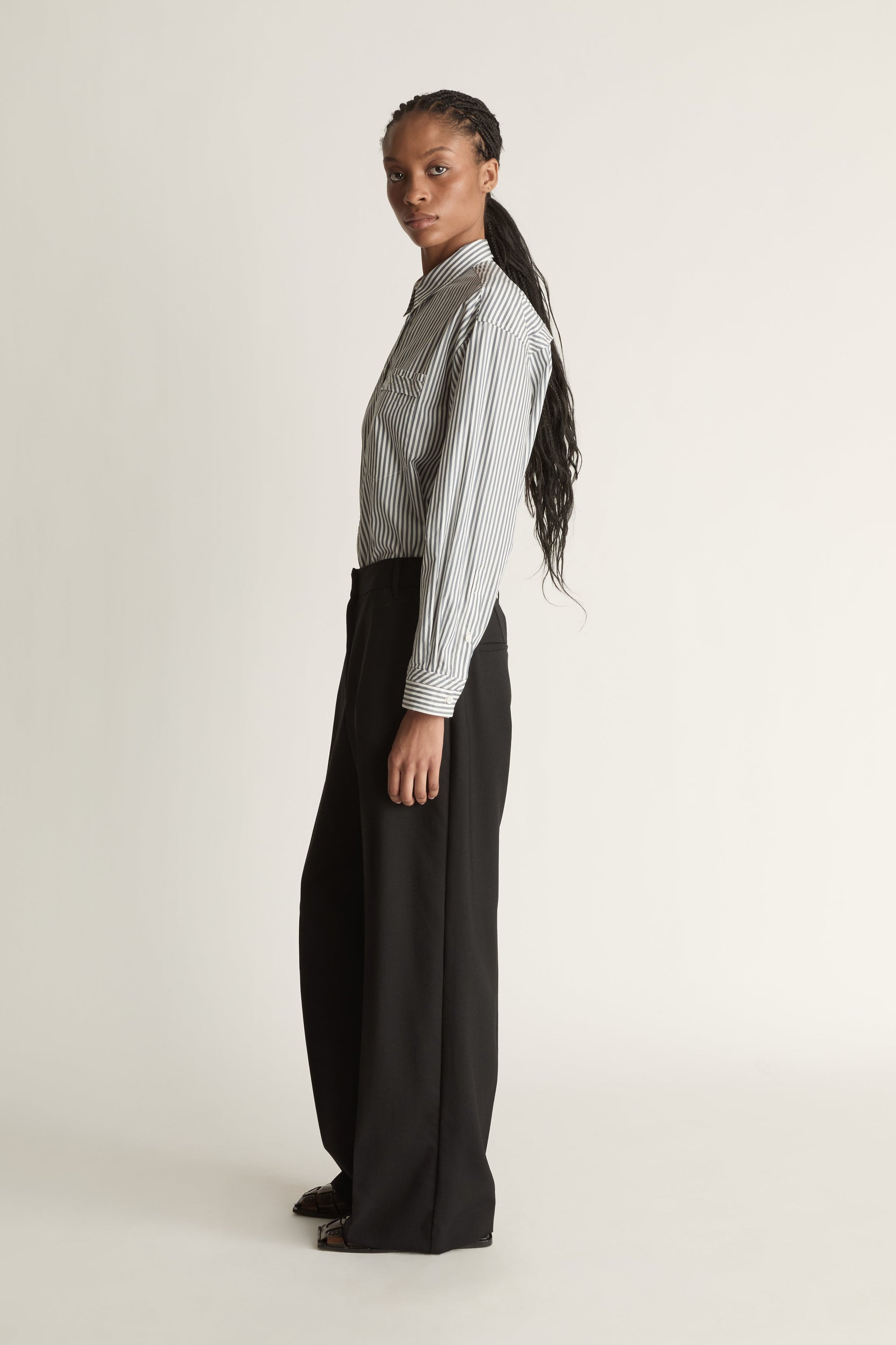 Person wearing a striped shirt and black pants on a white background