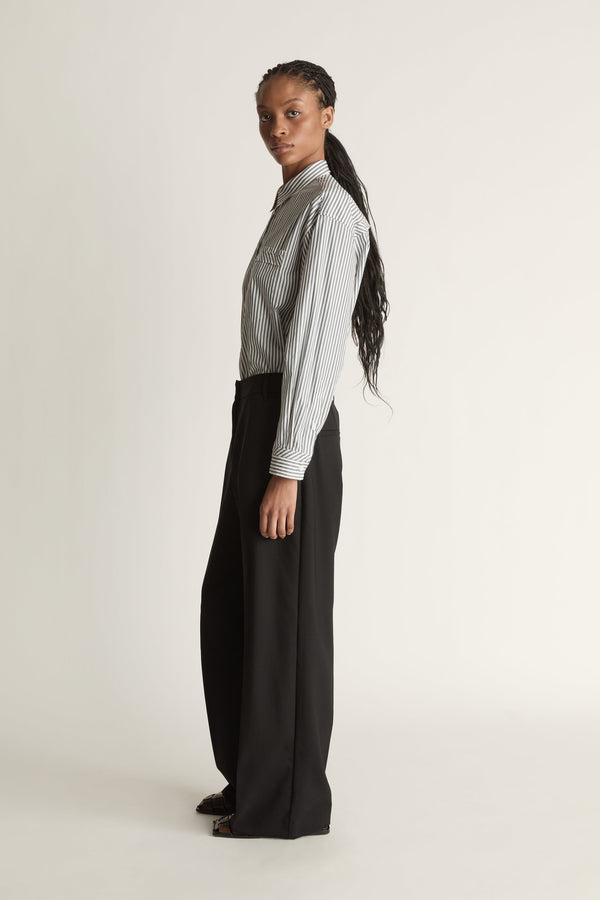 Person wearing a striped shirt and black pants on a white background