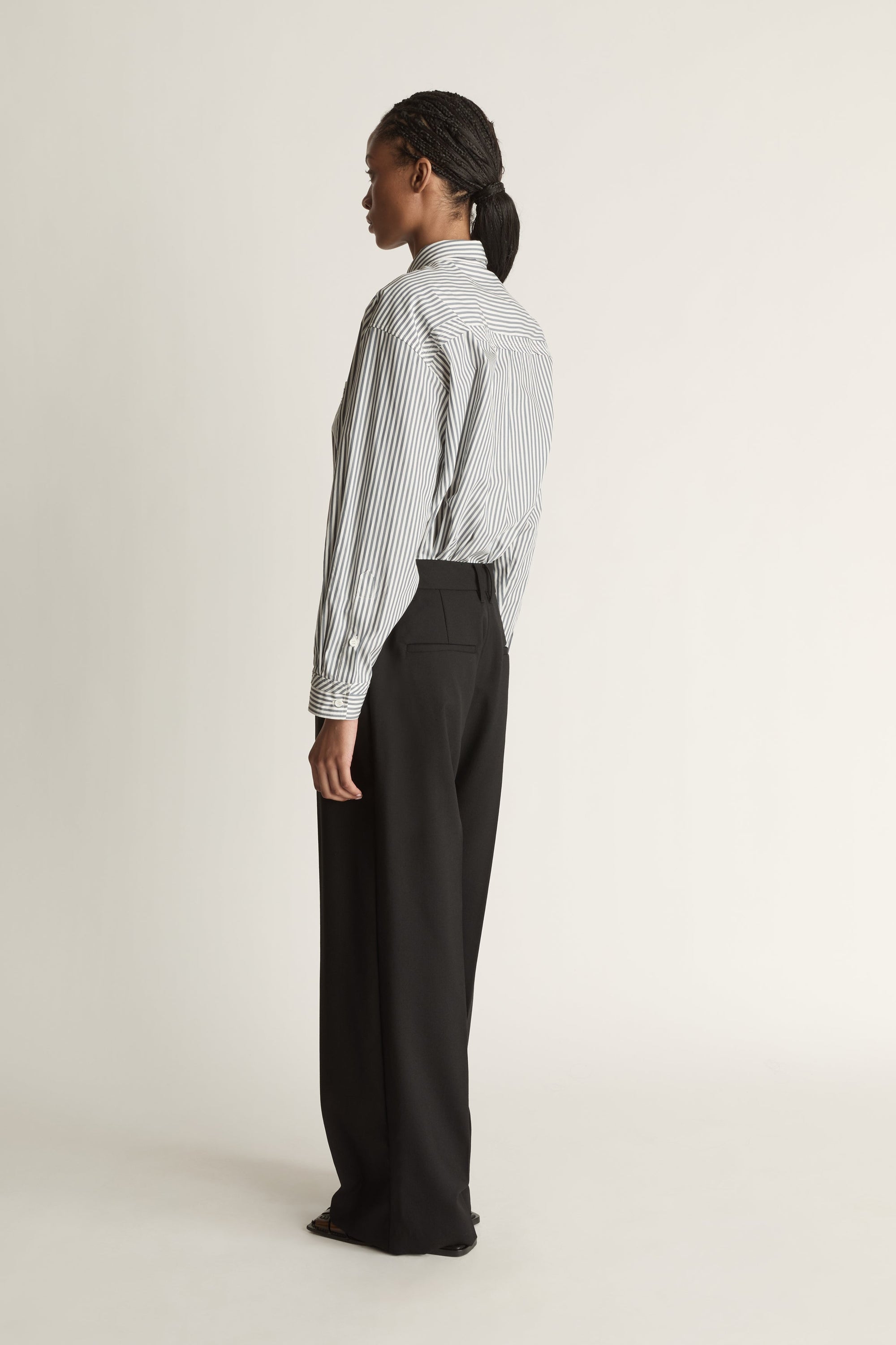 Person wearing a striped shirt and black pants on a white background