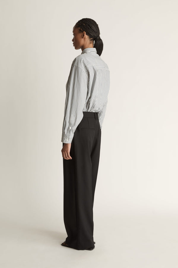 Person wearing a striped shirt and black pants on a white background