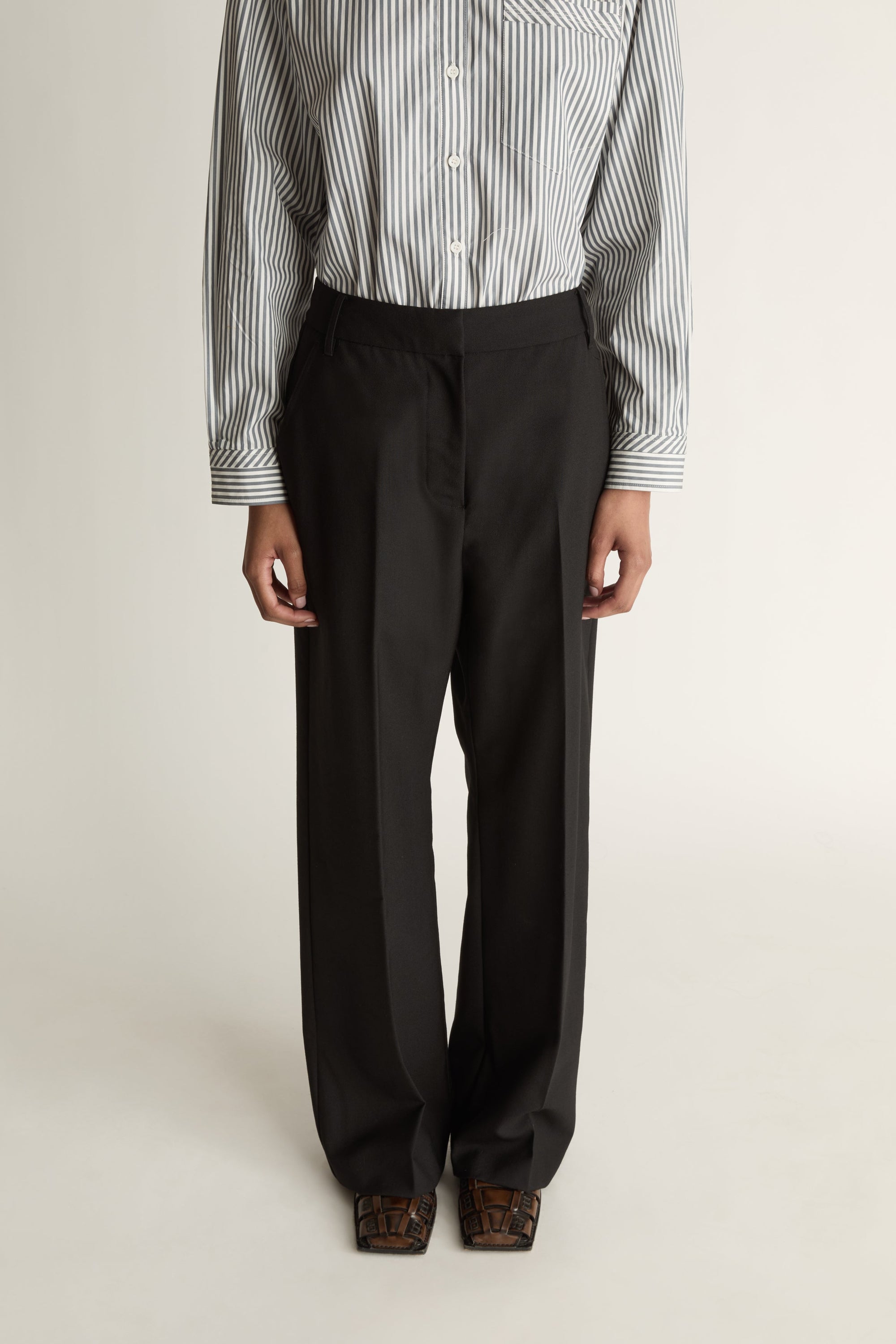 Person wearing a striped shirt and black pants on a white background