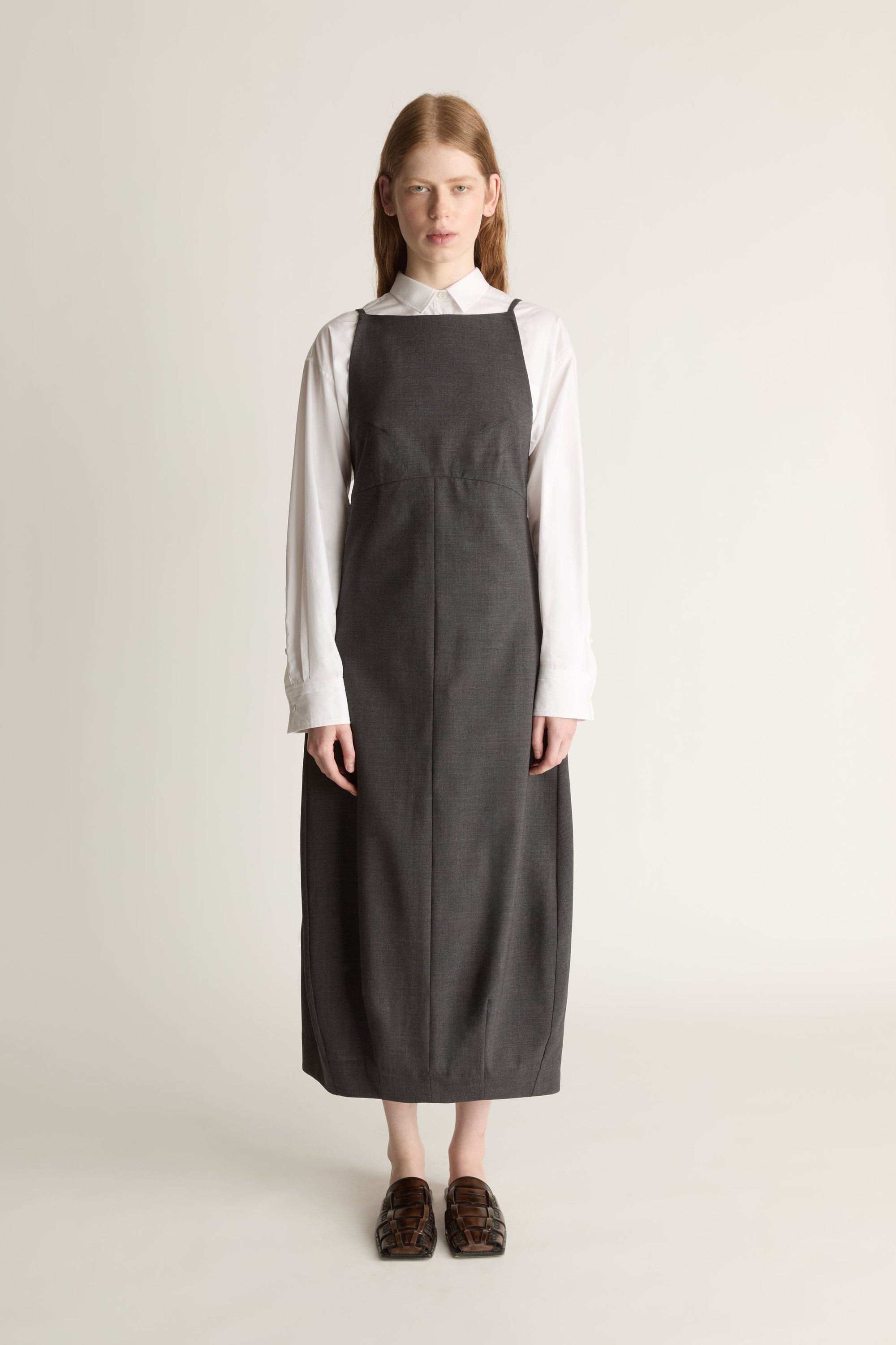 Person wearing a long dark apron style dress over a light shirt on a plain background