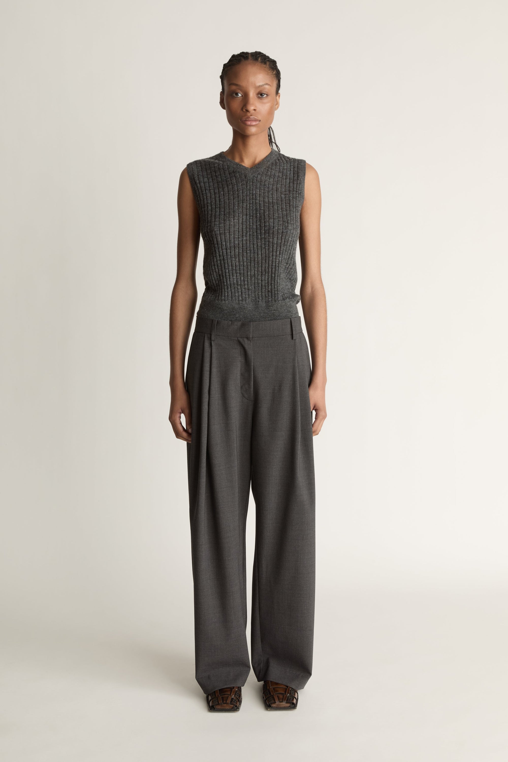 Woman wearing a sleeveless knitted top and wide-leg pants on a plain background