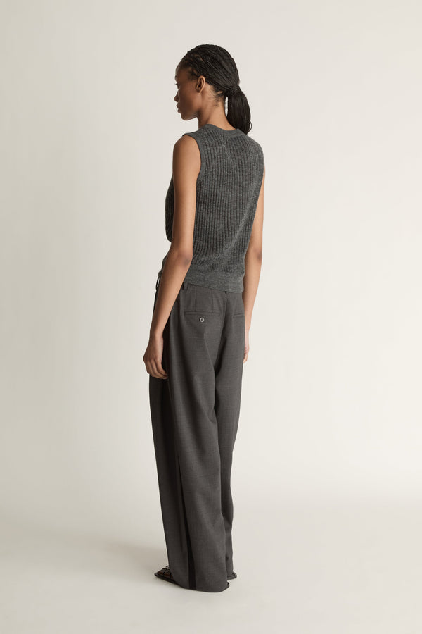 Woman wearing a sleeveless knitted top and wide-leg pants on a plain background