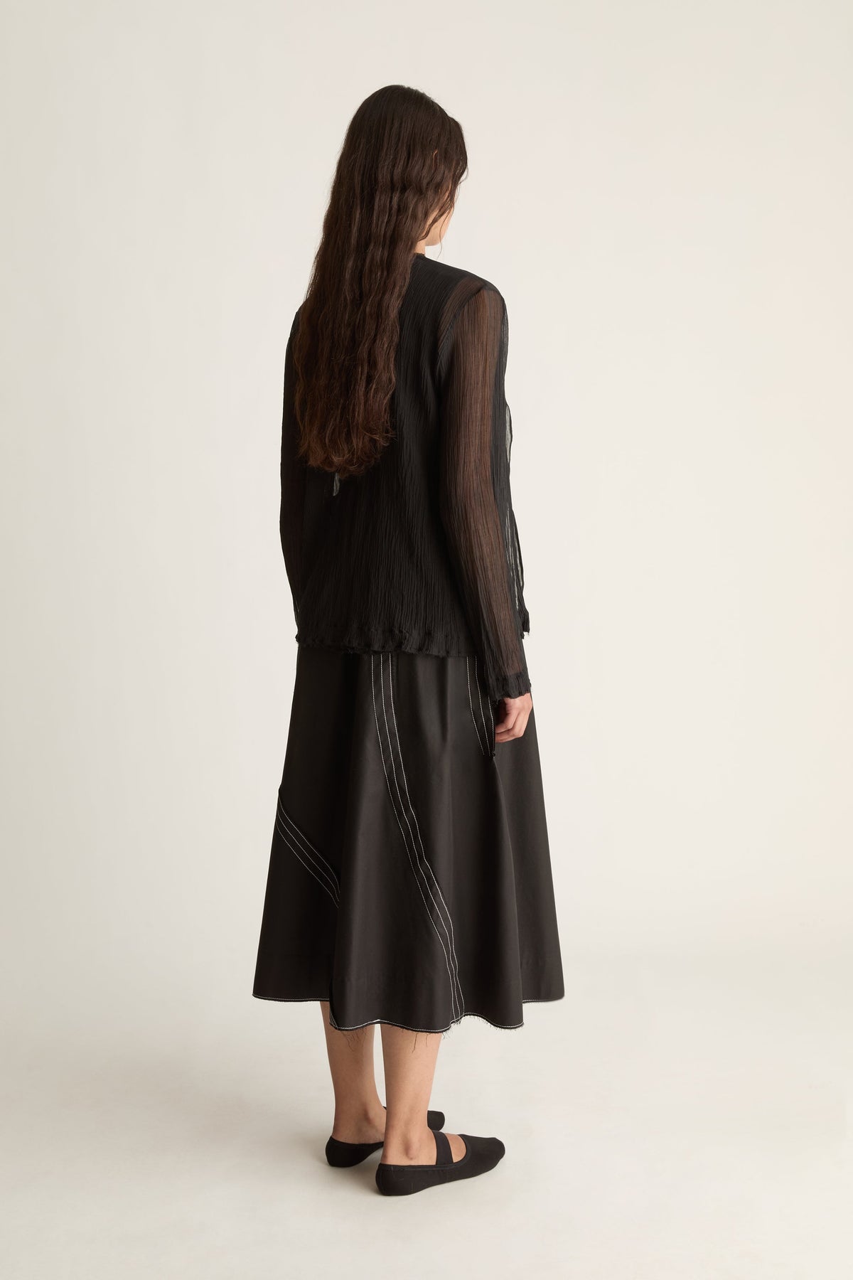 Back view of a woman with long wavy hair in a sheer black cardigan and black midi skirt