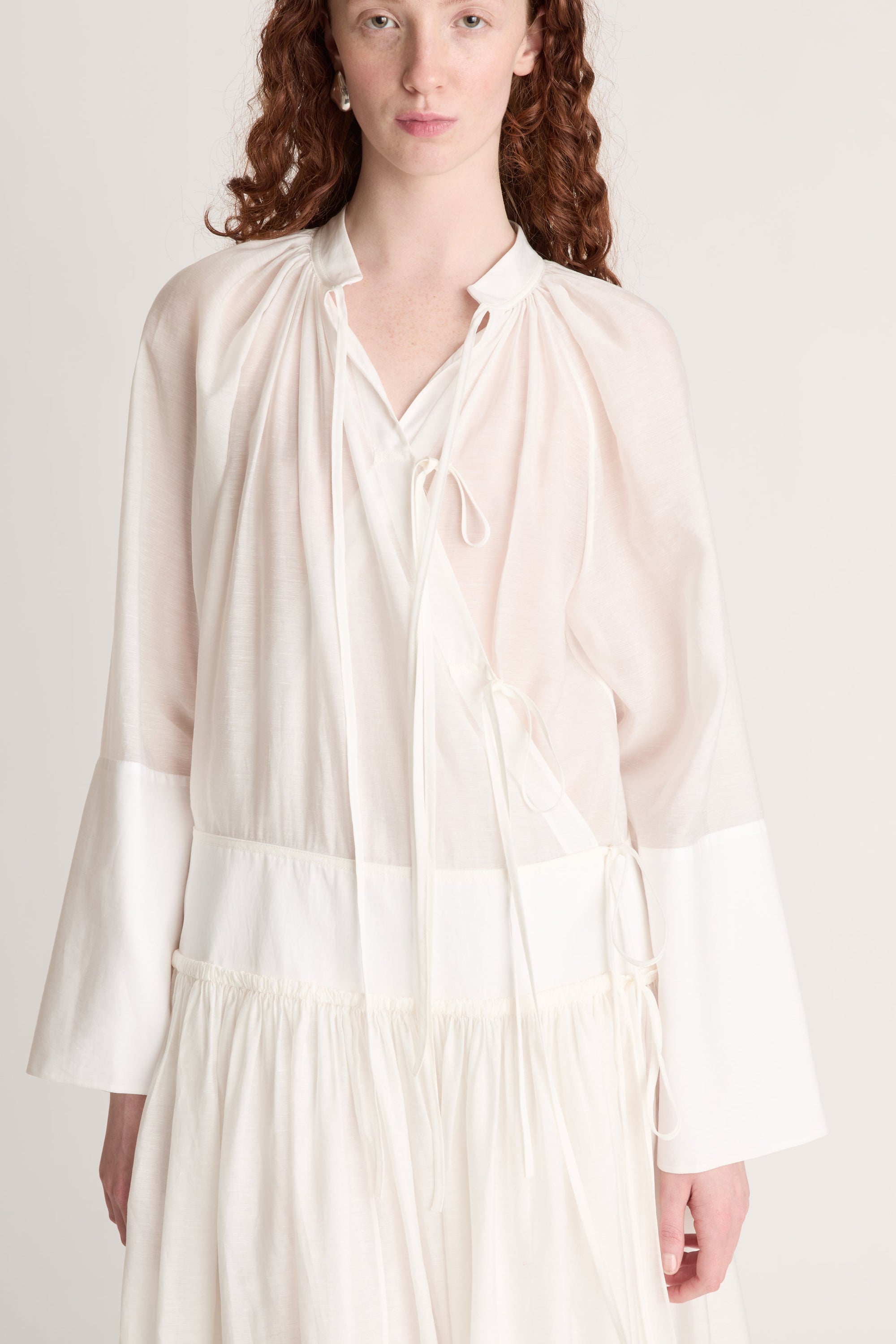 A woman wearing a long white dress with a tie detail, on a plain background
