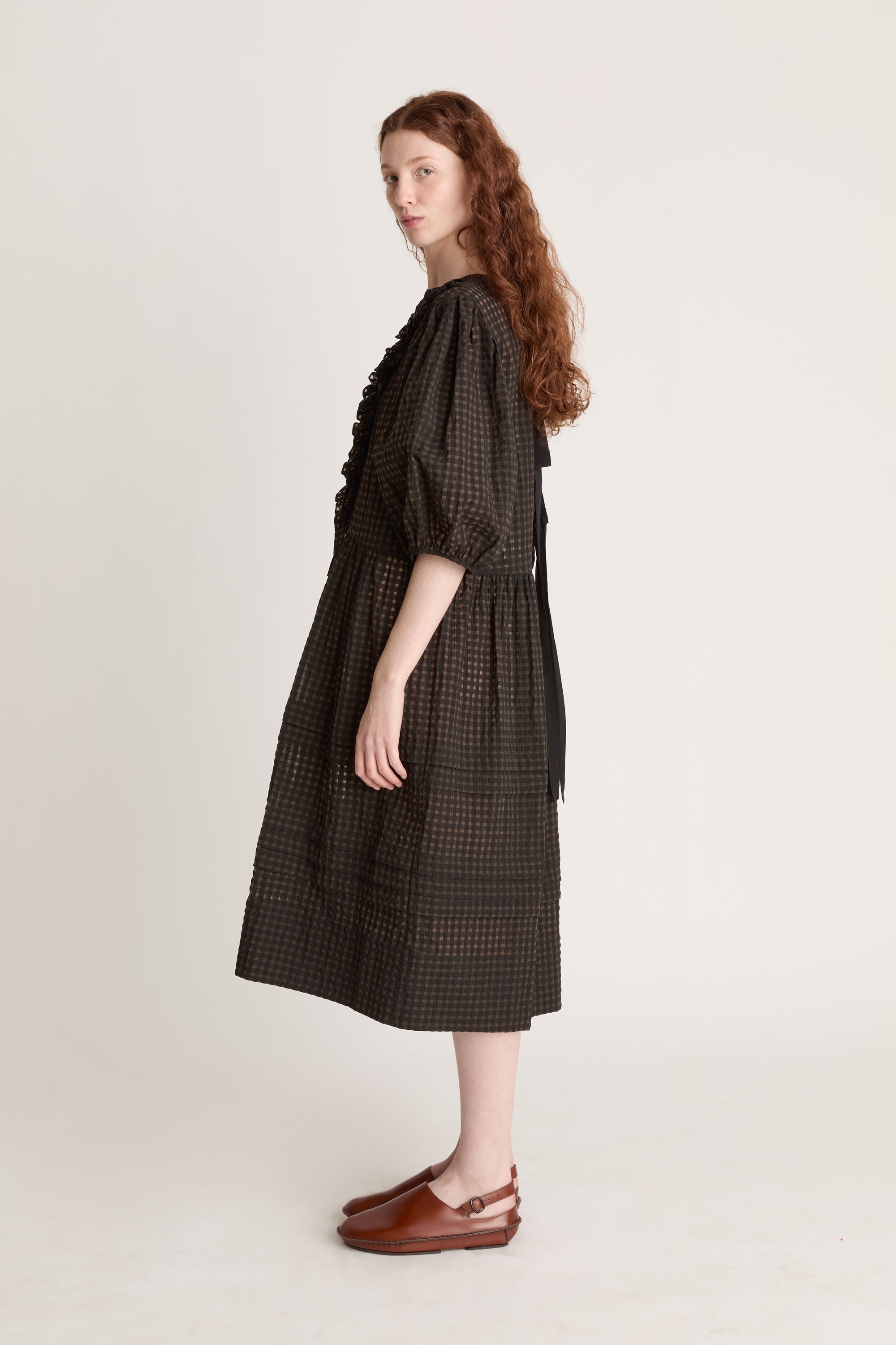Woman wearing a dark checkered dress  with puffy sleeves with ruffled details on a white background