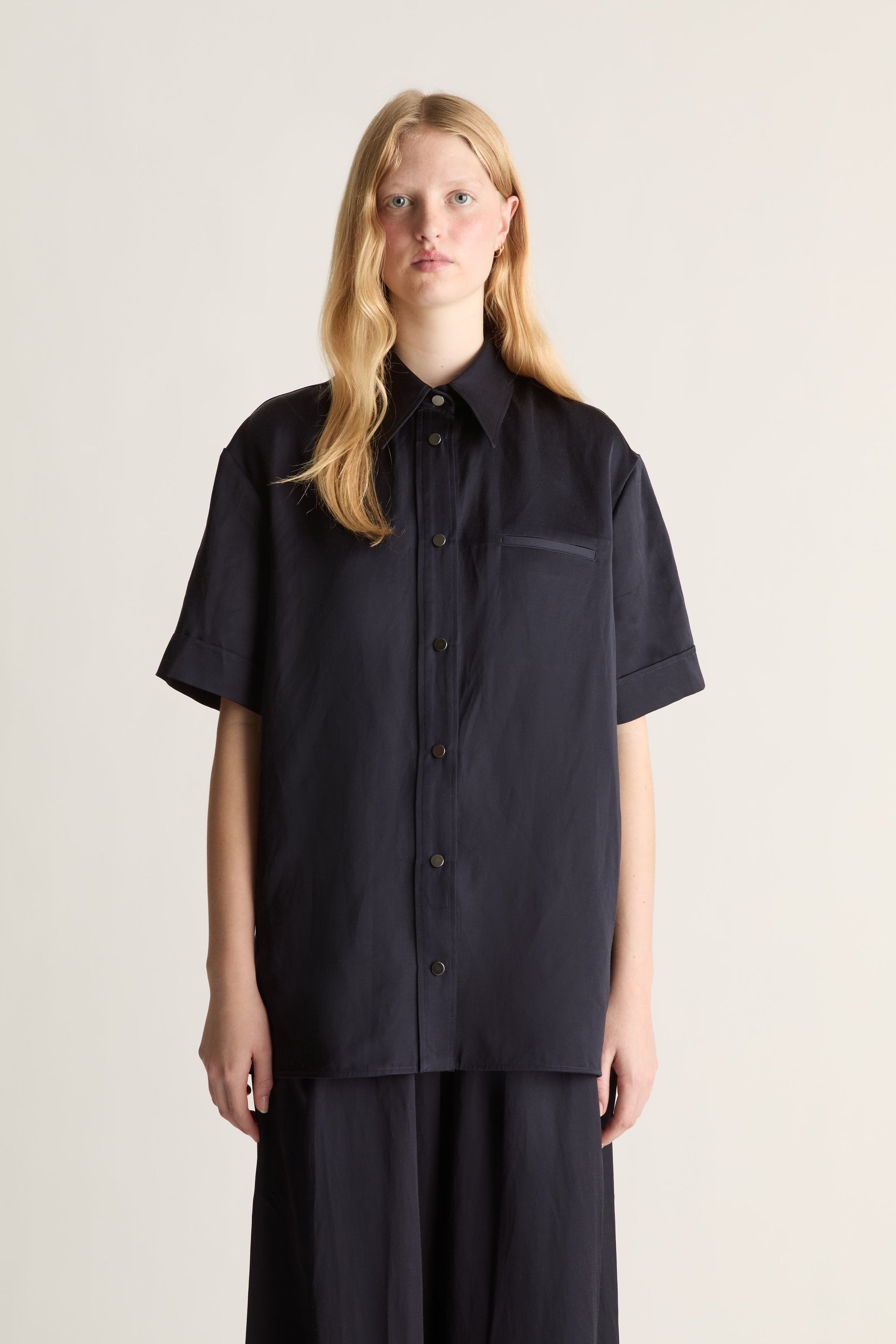 Close up of a woman wearing a navy short sleeve button up shirt and wide leg trousers. 