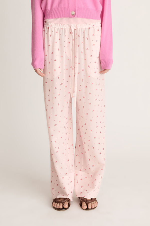 Woman wearing pink cashmere cardigan and pink floral pants on a white background