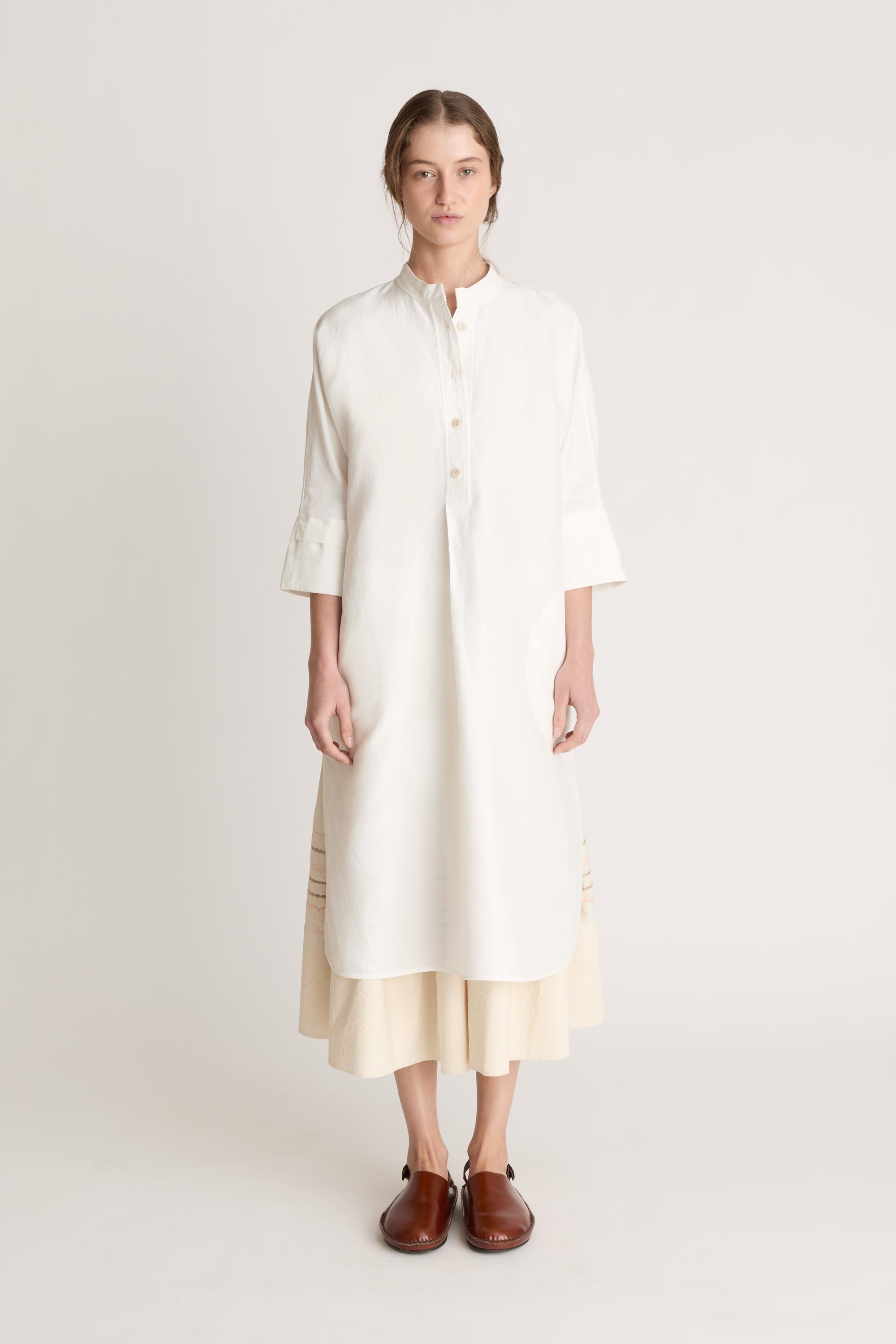 Woman wearing a white tunic with a beige skirt on a white background