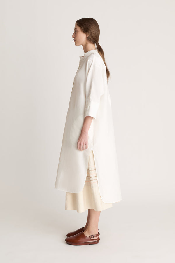 Woman wearing a white tunic with a beige skirt on a white background