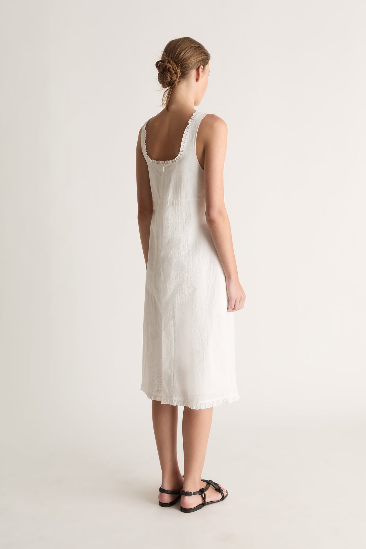 Back view of a woman with a low bun in a white dress with a ruffle-trimmed scoop back