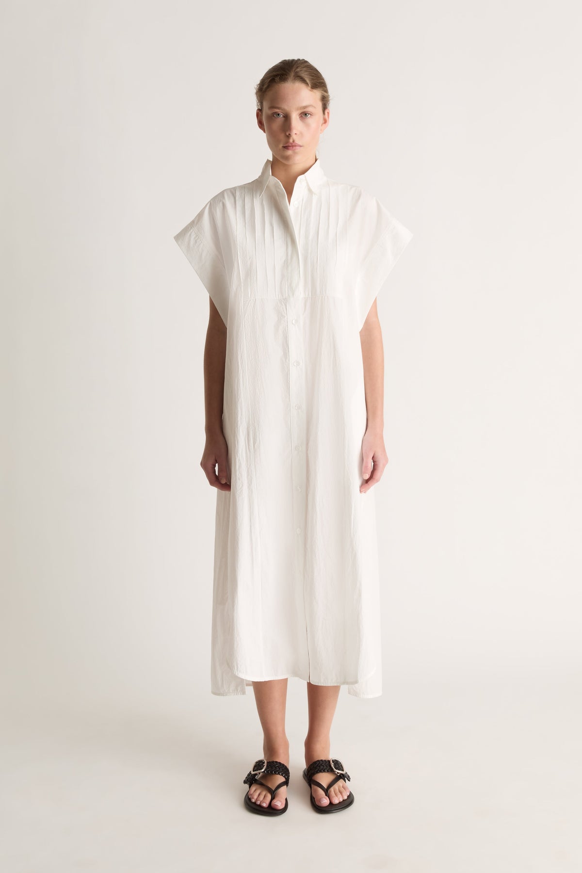 Front view of a white midi shirt dress with wide cap sleeves, a pin-tucked bib and button front.