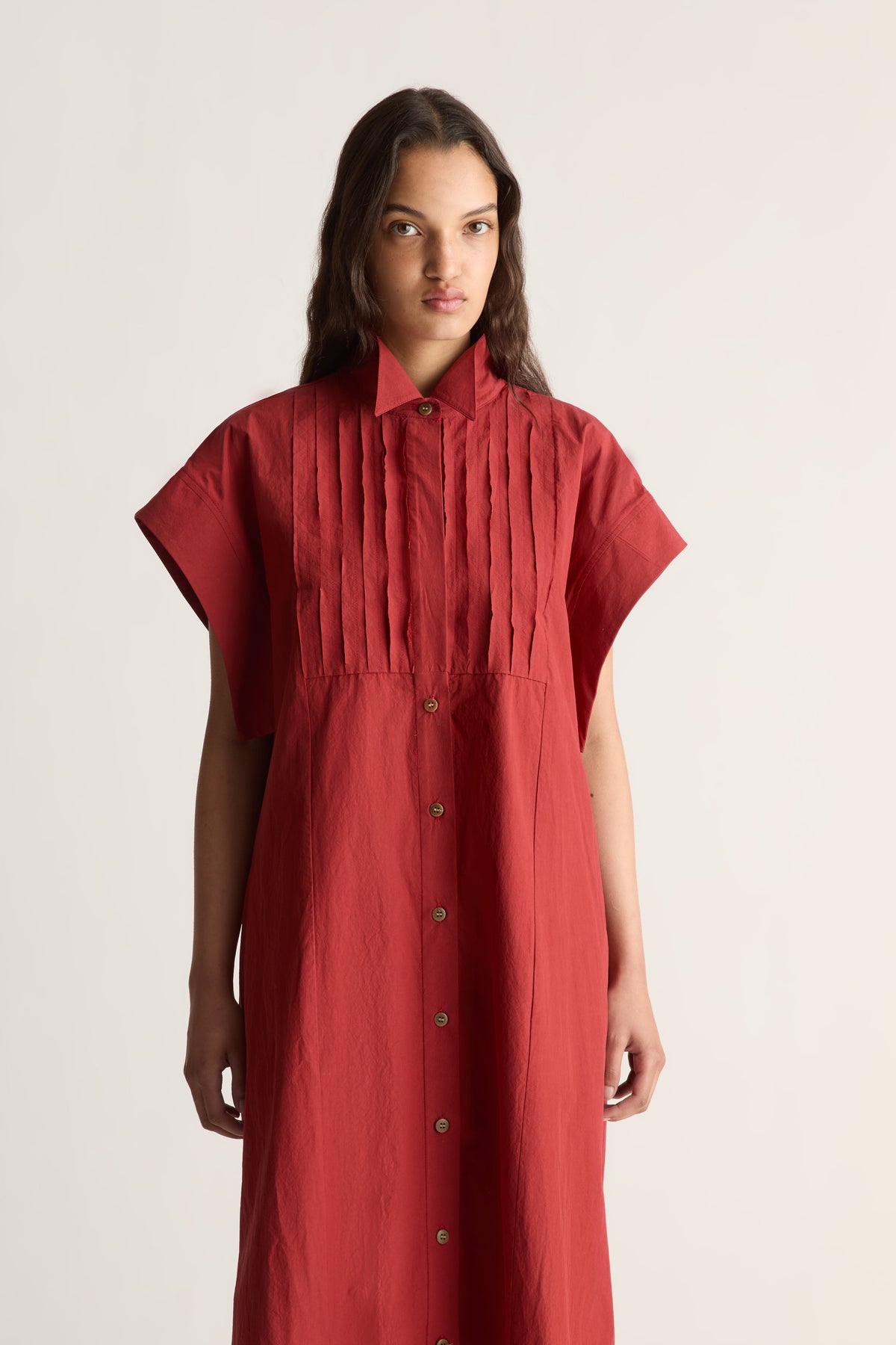 Close-up of a red shirt dress with pointed collar, pleated bib and button front