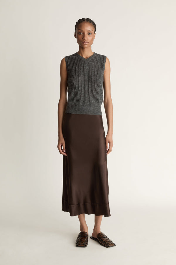 Woman wearing a sleeveless gray top and brown skirt on a plain background