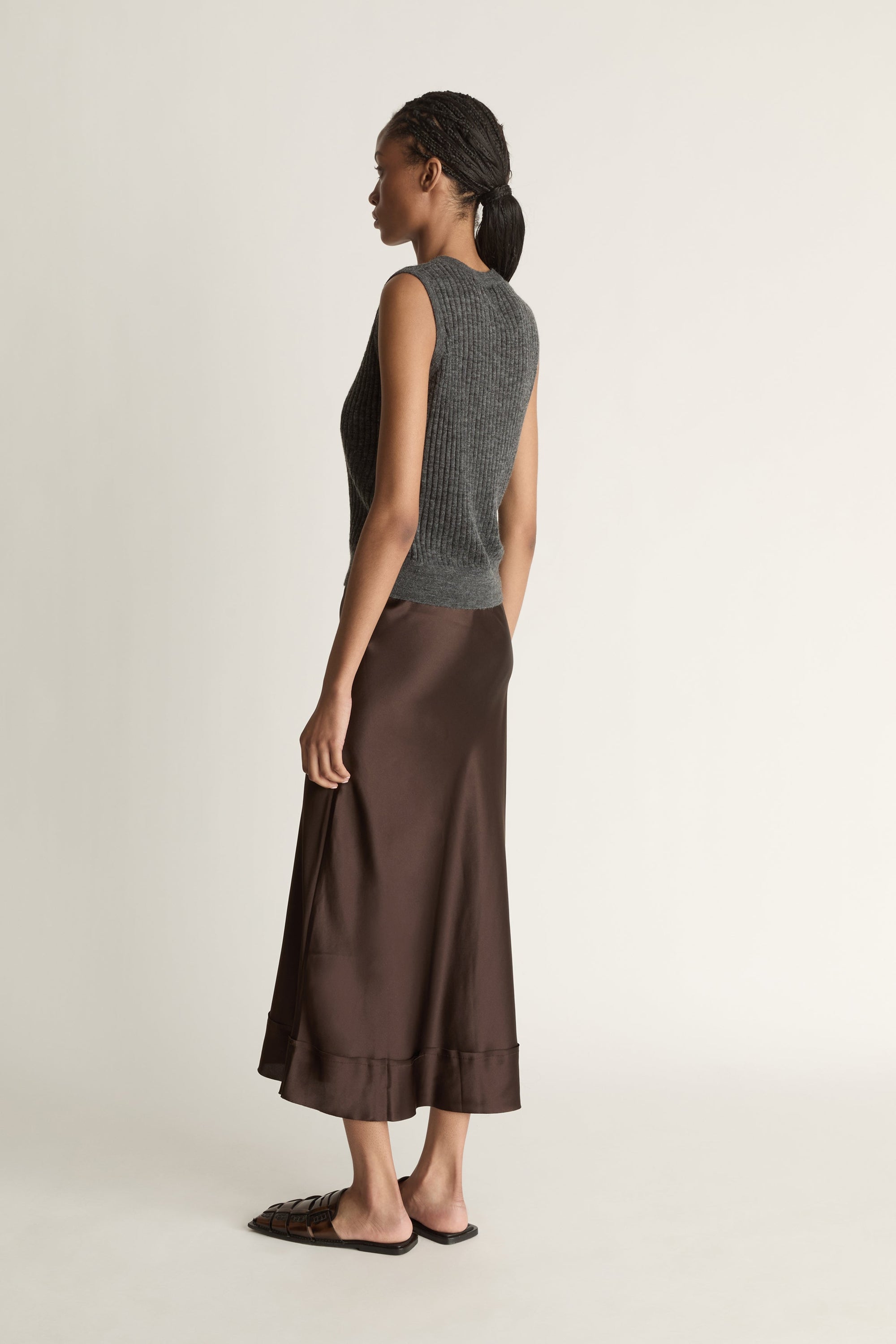 Woman wearing a sleeveless gray top and brown skirt on a plain background