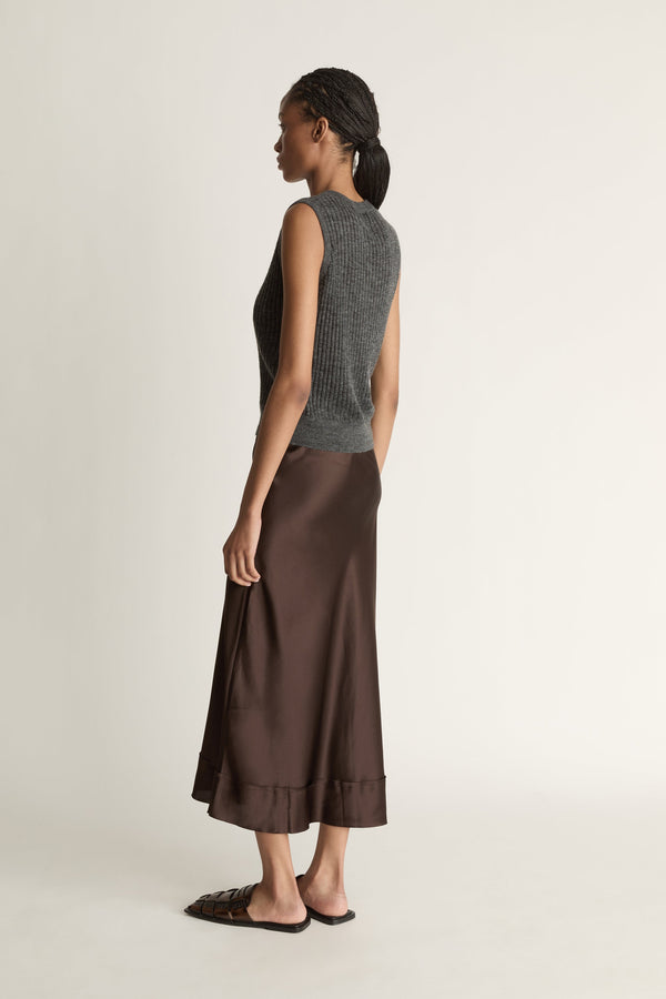 Woman wearing a sleeveless gray top and brown skirt on a plain background